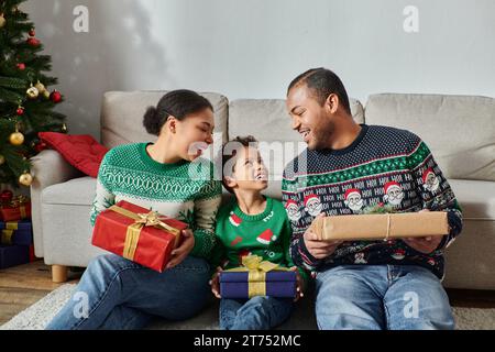 Joyeux parents afro-américains regardant avec amour leur fils et tenant des cadeaux, Noël Banque D'Images