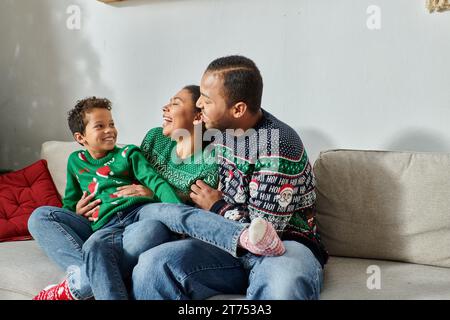 Joyeux parents afro-américains tenant leur fils sur des tours souriant heureux l'un à l'autre, Noël Banque D'Images