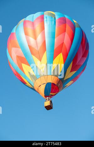 Une montgolfière aux couleurs vives avec un motif géométrique volant dans un ciel bleu clair. Banque D'Images