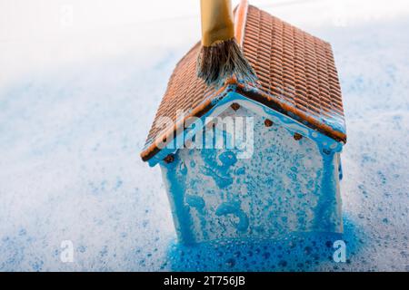 Petite maison modèle et une brosse à peinture dans de l'eau mousseuse Banque D'Images