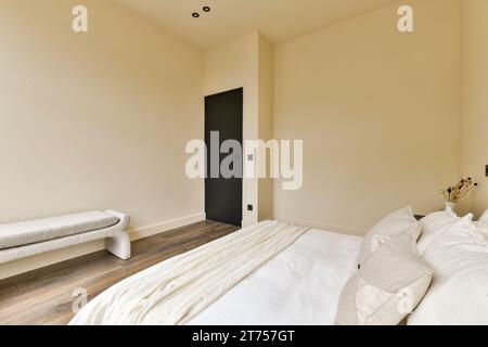 une chambre avec parquet et draps blancs sur le lit, il y a une porte noire dans la chambre Banque D'Images