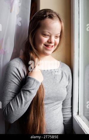 Fille souriante avec le syndrome de Down posant par la fenêtre Banque D'Images