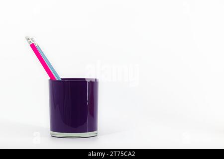 Un organiseur de bureau en verre violet sur fond blanc contient trois crayons avec des gommes dans les tons rose, bleu et marine. Banque D'Images