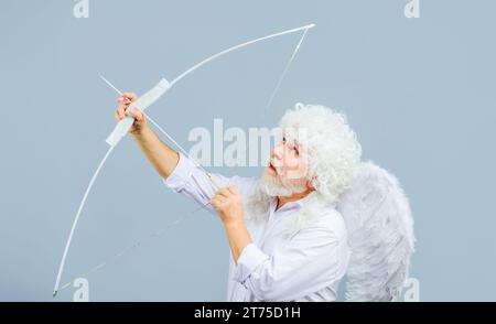 Bonne Saint Valentin. Homme barbu en perruque bouclée blanche et ailes d'ange tirant la flèche d'amour. Saint Valentin cupidon ange avec arc et flèche. Flèche d'amour Banque D'Images