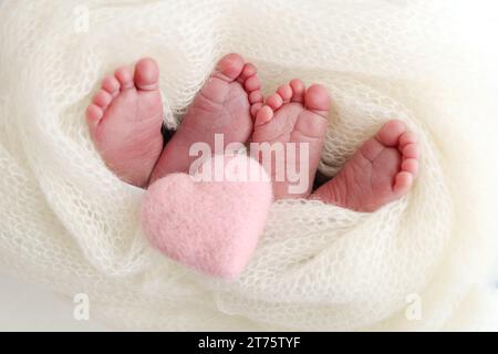 Pieds nouveau-né jumeaux deux paires de pieds de bébé dans une couverture tricotée blanche. Coeur rose Banque D'Images