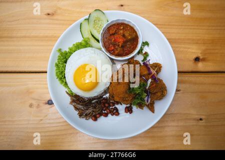 Nasi Lemak avec poulet frit et œuf sur une assiette blanche avec concombre Banque D'Images