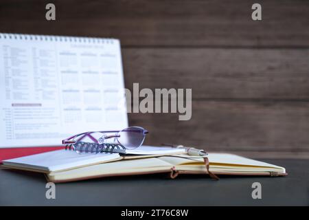 Lunettes sur le dessus des blocs-notes à côté du calendrier de bureau. Sur fond de mur en bois. Espace de copie Banque D'Images