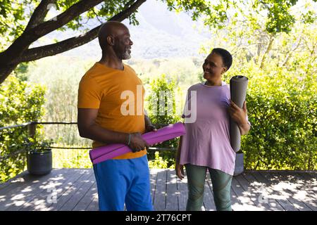Heureux divers amis seniors masculins et féminins parlant à la classe de yoga dans le jardin ensoleillé Banque D'Images