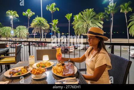 Pattaya Thaïlande 10 novembre 2023, Hard rock café et hôtel sur la route de la plage au coucher du soleil avec des cocktails sur la table, femme dînant dans la soirée Banque D'Images