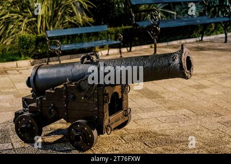 Vieux canon en bronze sur un chariot en bois avec des roues se tient sur les pavés près du banc Banque D'Images