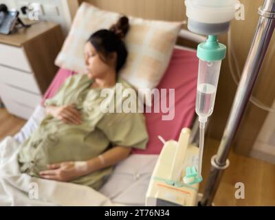 Goutte à goutte de solution saline médicale IV avec femme enceinte reposant sur un lit à l'hôpital Banque D'Images