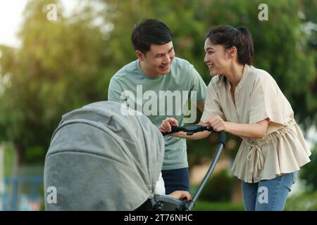 parent heureux (père et mère) parlant et jouant avec bébé bébé en poussette tout en se reposant dans le parc Banque D'Images