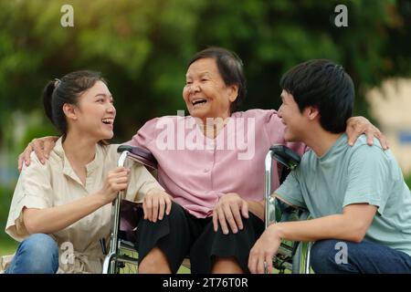 heureux petit-fils et petite-fille parlant avec la femme âgée en fauteuil roulant au parc Banque D'Images