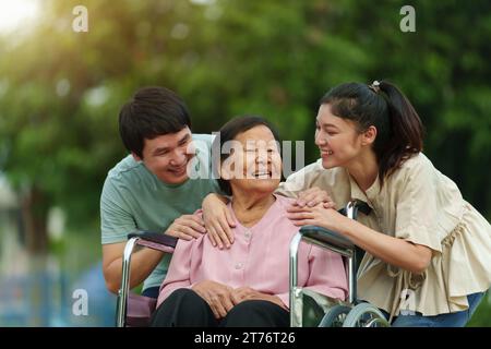 heureux petit-fils et petite-fille parlant avec la femme âgée en fauteuil roulant au parc Banque D'Images