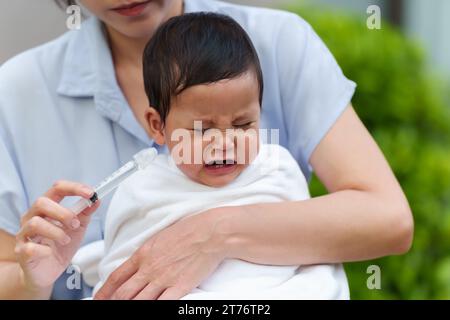 mère faisant le lavage nasal pour son bébé qui pleure avec seringue et solution saline. nettoyer le nez de bébé Banque D'Images