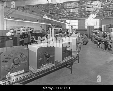 Travailleurs sur la chaîne de production d'un fabricant de produits électriques de divertissement à domicile aux États-Unis c.1960. Le convoyeur central a des téléviseurs en cours d'assemblage (inhabituellement logés dans un boîtier métallique). Les écrans de moniteur (CRT) qui sont assemblés dans les unités extérieures des téléviseurs se trouvent sur la droite. Sur la gauche, la ligne de production produit des radiogrammes ou des consoles, des unités en bois avec des pieds. Les unités tourne-disques sont empilées à côté de la ligne. Dans les cases à droite dans le coin indiquent que ces composants ont été fournis par V-M («Voice of Music») de Benton Harbor, Michigan. Banque D'Images