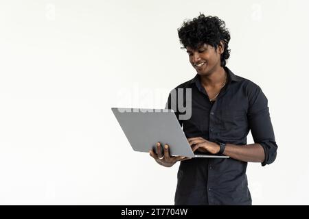 Toujours prêt à aider. Confiant jeune homme indien tenant l'ordinateur portable et souriant tout en se tenant sur fond blanc Banque D'Images