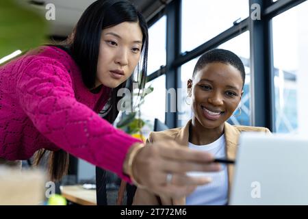 Heureux collègues féminins divers utilisant l'ordinateur portable et parlant au bureau dans le bureau Banque D'Images