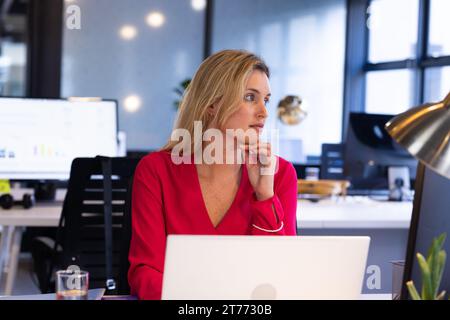 Homme d'affaires caucasien décontracté réfléchi utilisant un ordinateur portable assis au bureau, regardant loin dans le bureau Banque D'Images
