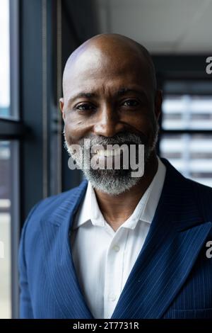 Portrait d'homme d'affaires afro-américain chauve avec barbe souriant par la fenêtre dans le bureau Banque D'Images