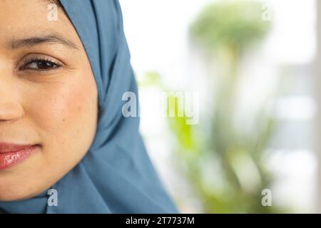 Demi portrait de femme biracial heureuse dans le hijab à la maison ensoleillée avec espace de copie Banque D'Images