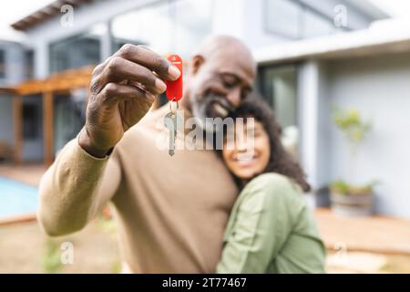 Heureux couple diversifié tenant les clés de la maison embrassant en dehors de la nouvelle maison Banque D'Images