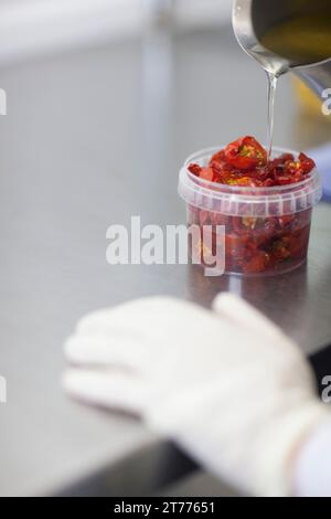 Close up d'un travailleur part versez de l'huile dans un récipient en plastique rempli de tomates séchées au soleil Banque D'Images