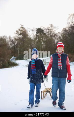 Portrait de deux garçons marcher dans la neige tirant un traîneau Banque D'Images