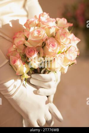 Close up of a les mains gantées tenant un bouquet de roses Banque D'Images