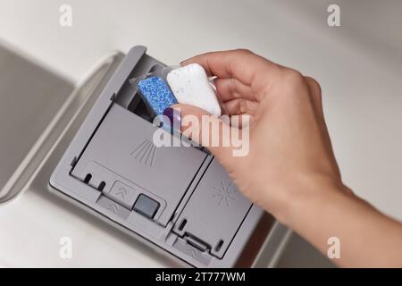 main féminine met la tablette de lave-vaisselle dans la machine à lave-vaisselle intégrée automatique ouverte. Gros plan Banque D'Images