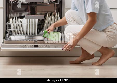 la main féminine verse le liquide de rinçage dans le compartiment lave-vaisselle de la cuisine blanche moderne Banque D'Images