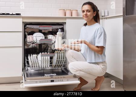 femme verse le liquide de rinçage dans le compartiment lave-vaisselle dans la cuisine blanche moderne Banque D'Images