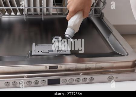 la main féminine verse le liquide de rinçage dans le compartiment lave-vaisselle de la cuisine blanche moderne Banque D'Images