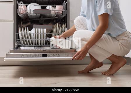 la main féminine verse le liquide de rinçage dans le compartiment lave-vaisselle de la cuisine blanche moderne Banque D'Images