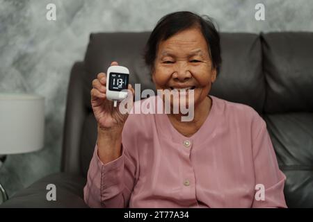 heureuse femme âgée tenant le glucomètre avec le résultat de la mesure du sucre bon niveau. vérifiez le concept de diabète. Banque D'Images