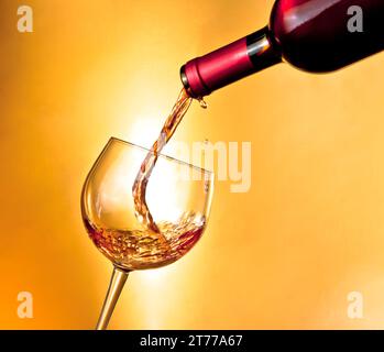 commencez à remplir le vin rouge dans le verre incliné sur fond doré Banque D'Images