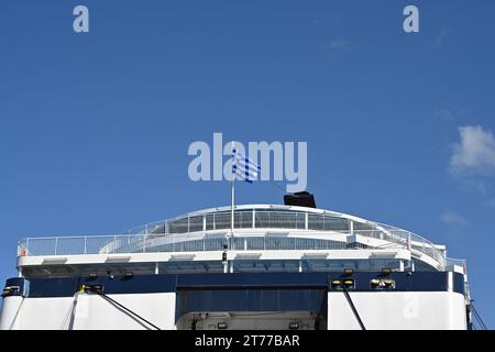 La partie arrière du ferry de passagers avec la coque bleue et blanche et le drapeau grec sur le dessus est observée contre le ciel clair. Banque D'Images