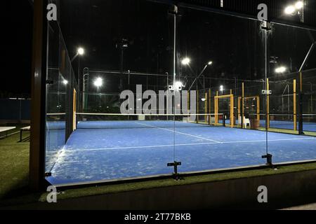 Court bleu clos éclairé pour padel pendant la nuit avec construction créée par le maillage et les murs arrière en verre. Banque D'Images