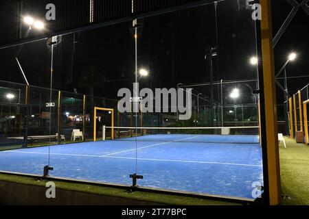 Vue de nuit sur cour bleue fermée pour padel avec construction créée par maille et les murs arrière en verre. Banque D'Images