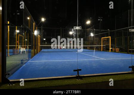 Une cour bleue fermée pour padel dans la nuit avec la construction créée par la maille et les murs arrière en verre. Banque D'Images