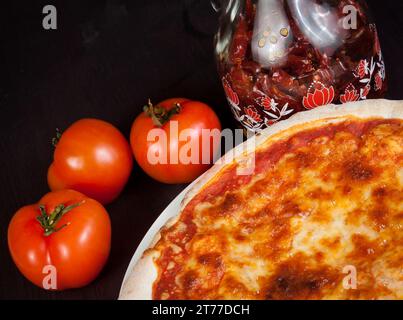 Délicieuse pizza fraîche près des tomates et huile épicée servie sur une table en bois Banque D'Images