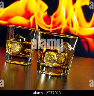 deux verres de whisky avec des glaçons devant la flamme sur la table en bois Banque D'Images