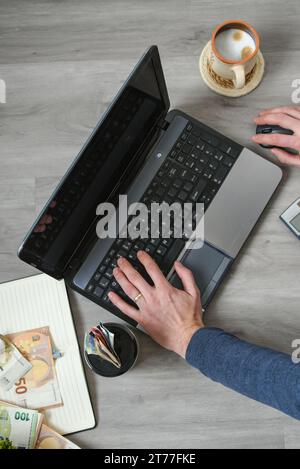 Mains d'homme travaillant sur ordinateur portable, vue de dessus, ordinateur portable, argent et café sur la table en bois Banque D'Images