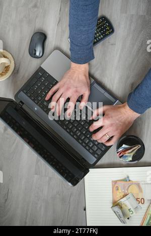 Mains d'homme travaillant sur ordinateur portable, vue de dessus, ordinateur portable, argent et café sur la table en bois Banque D'Images
