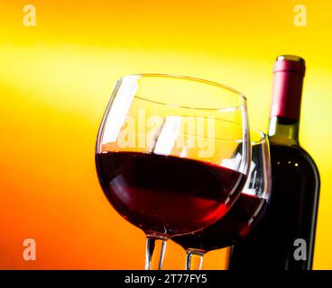 deux verres à vin rouge près de la bouteille sur fond de lumières dorées, concept festif et amusant Banque D'Images