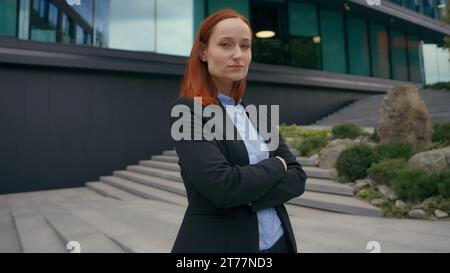 Portrait forte pose confiante femme d'affaires caucasienne aux cheveux rouges gingembre posant en ville à l'extérieur au milieu d'un immeuble de bureaux urbain moderne Banque D'Images