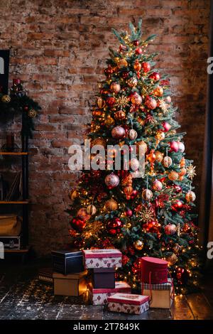 Sapin de Noël orné avec une riche gamme de décorations rouges et dorées, niché dans un cadre rustique avec des cadeaux Banque D'Images