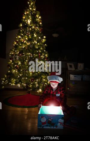 Enfant ouvrant cadeau de Noël sous l'arbre de Noël Banque D'Images