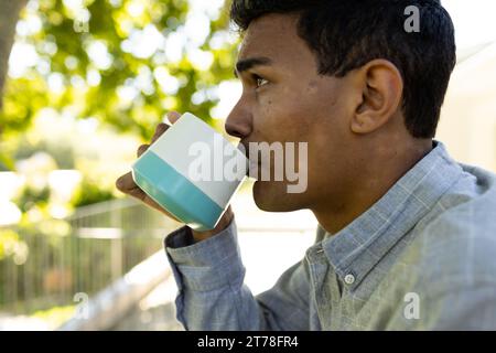 Homme biracial réfléchi buvant du café et debout sur le balcon à la maison Banque D'Images