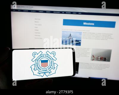 Personne tenant le smartphone avec le sceau de la Garde côtière des États-Unis (USCG) devant le site Web. Concentrez-vous sur l'affichage du téléphone. Banque D'Images